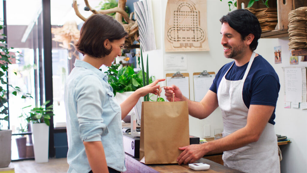 Smiling customer receiving a takeaway bag from a store worker.